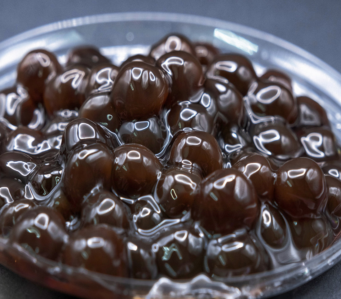 A close-up image of tapioca boba pearls, glossy and dark brown, presumably cooked and ready for use in bubble tea.