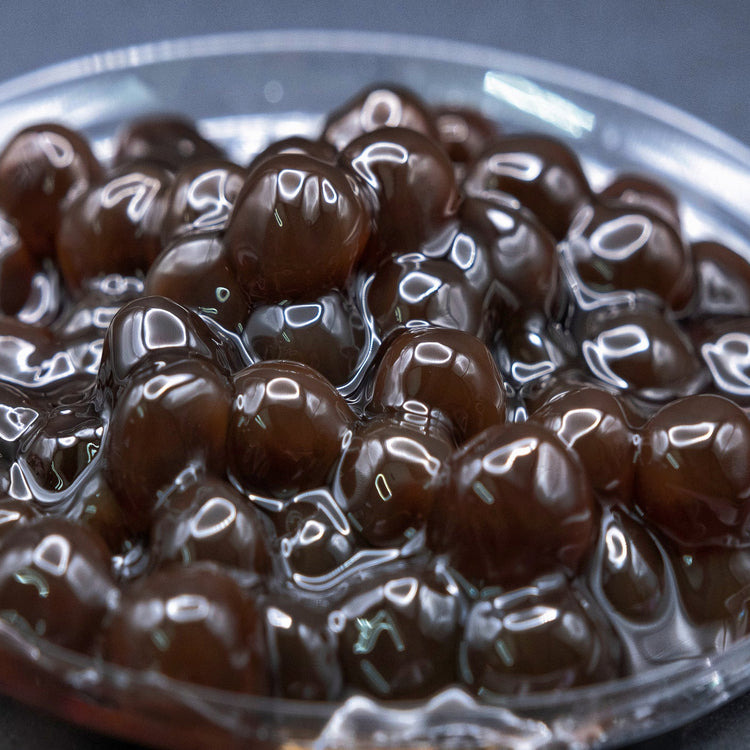 A close-up image of tapioca boba pearls, glossy and dark brown, presumably cooked and ready for use in bubble tea.