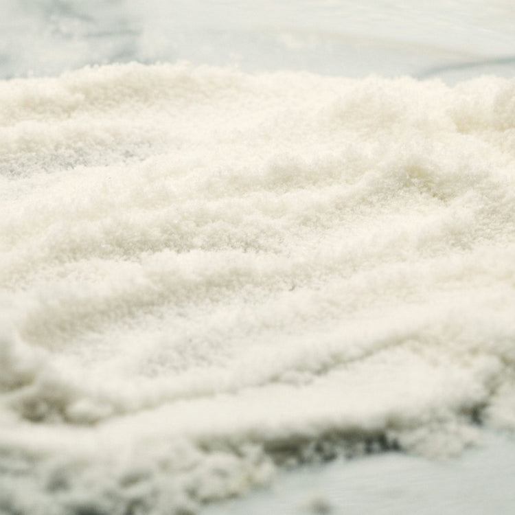 A mound of fine, off-white coconut powder piled on a light-colored surface, showing a soft, warm white hue.